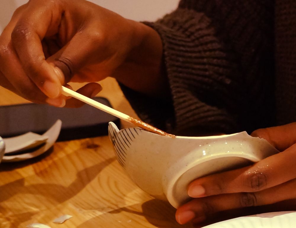Hands applying gold glue to pottery in a kintsugi class