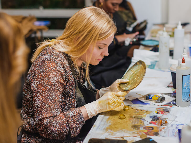 A woman is joining a broken plate together with gold adhesive at a kintsugi class