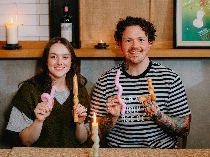Two people are smiling and holding up bendy candles made at a Bendy Boy class