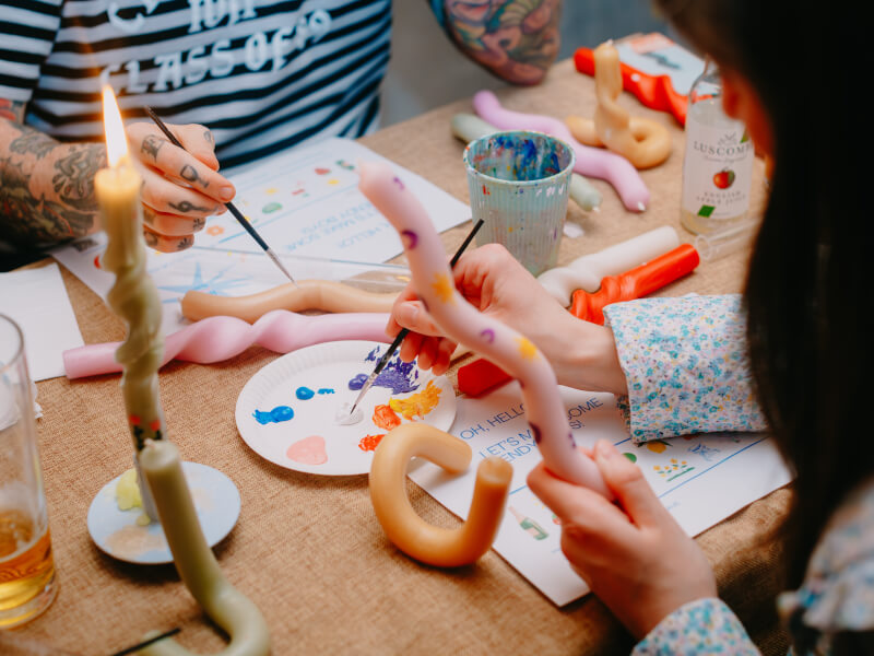 A close up of two people decorating bendy candles using paint