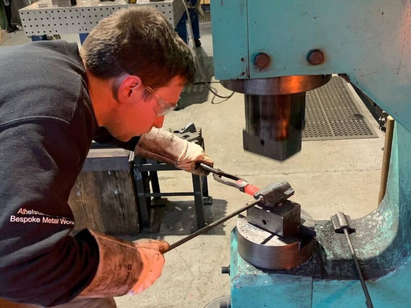 A man is using a tool to beat a piece of red hot metal into shape