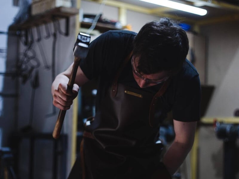 A man at a blacksmithing class is hitting white hot metal with a hammer