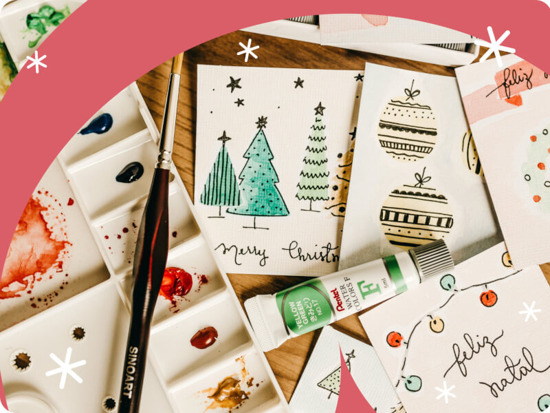Painted watercolour Christmas cards next to a paintbrush and a tube of paint.