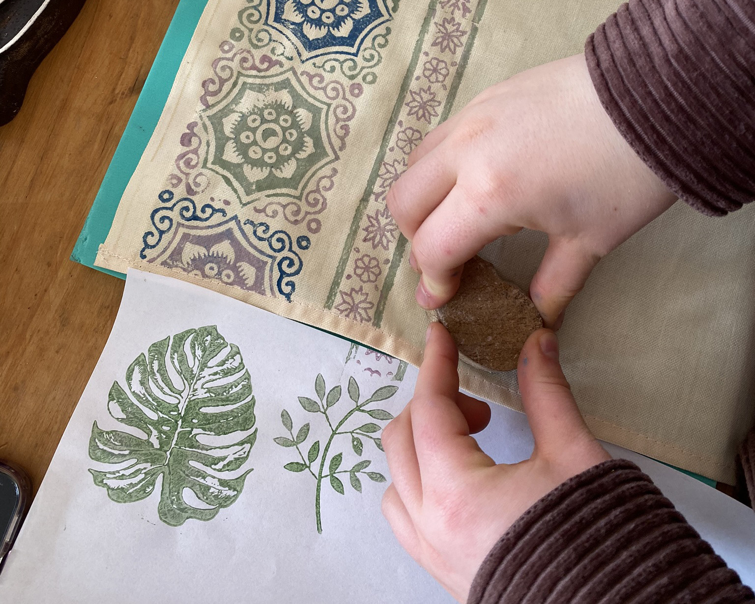 A close up of a person printing onto fabric using a wooden block