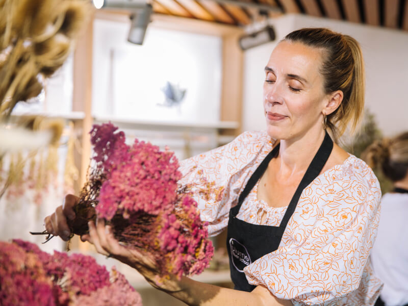 A woman is arranging large bunches of pink flowers in a vase