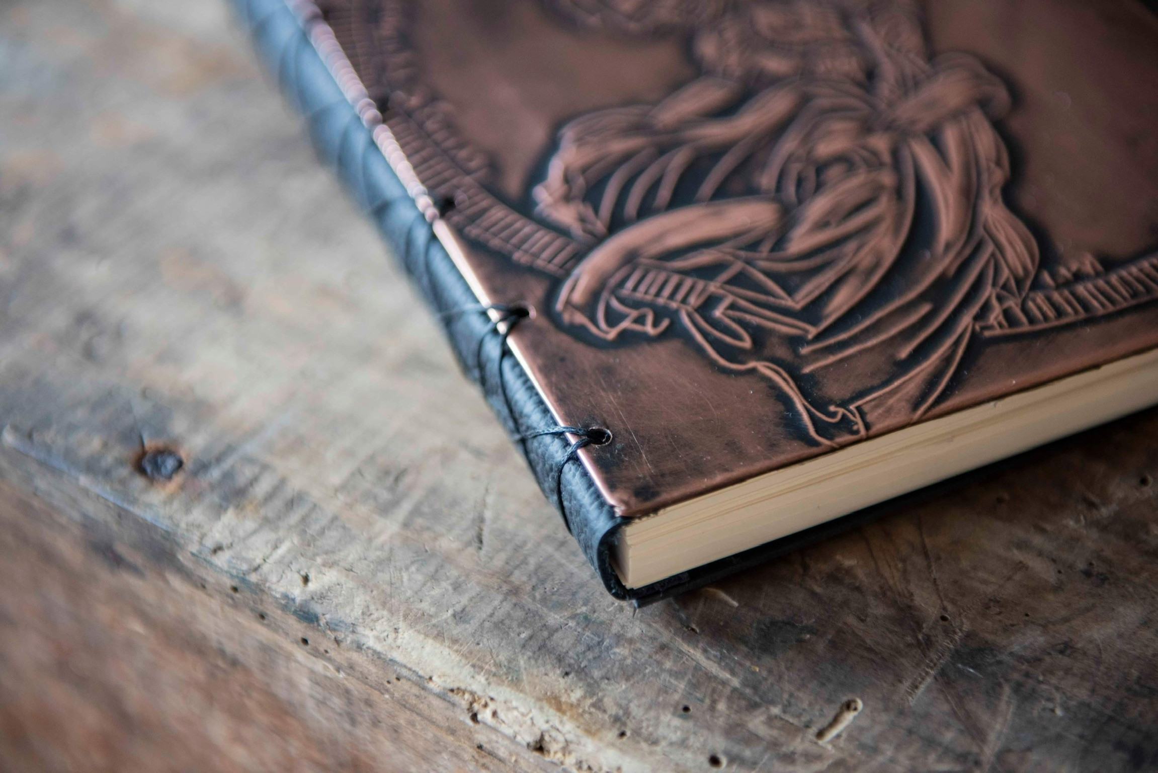 A handmade copper embossed journal sits on a wooden table