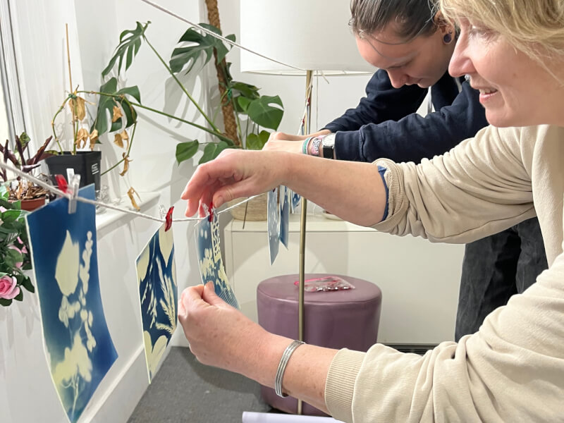 Two women are rinsing and pegging up cyanotype prints to dry