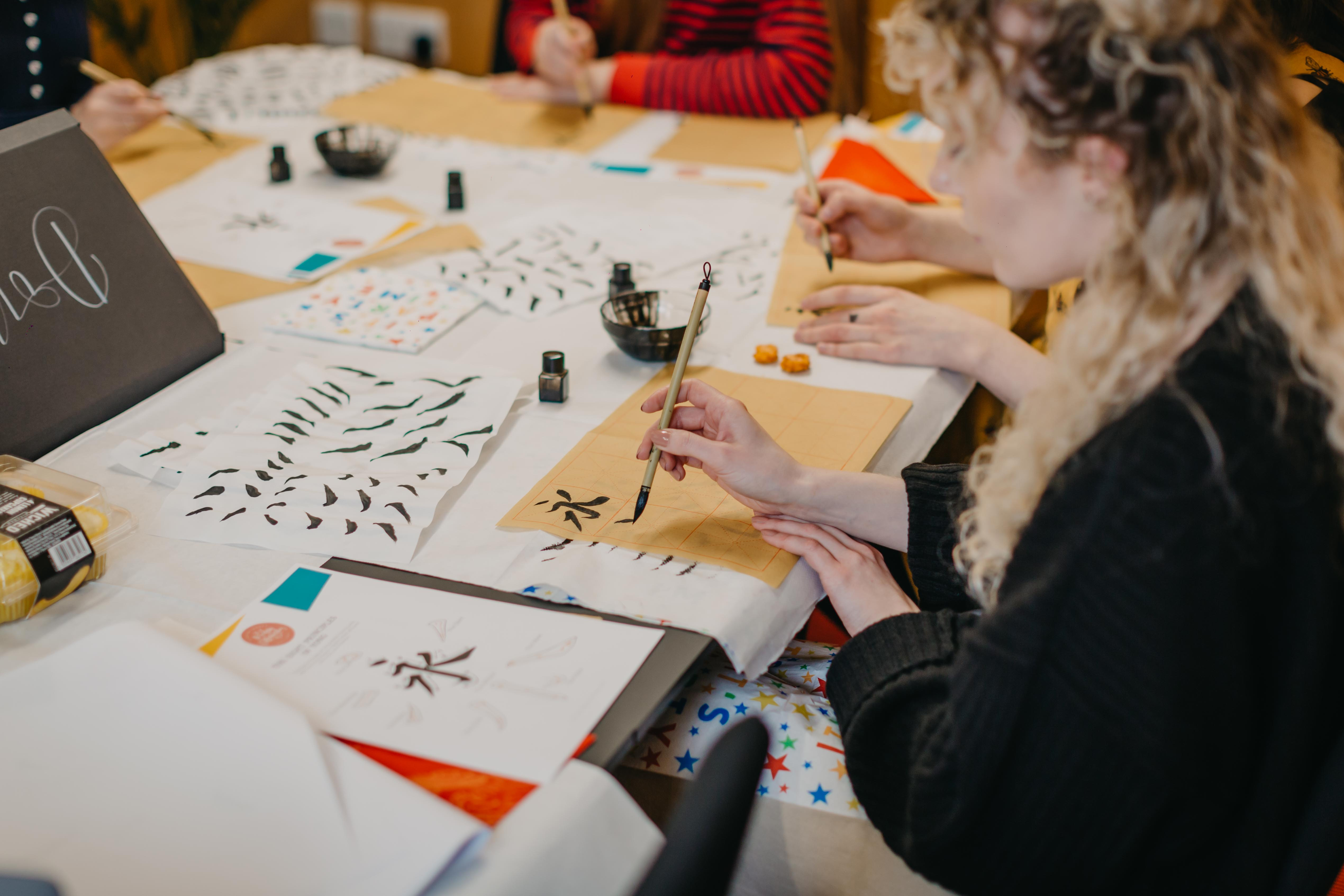 A group of people are learning how to do traditional brush lettering with brushes and ink
