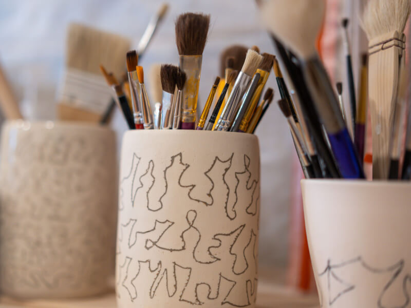 Three pots of paintbrushes stand on the side at an art class in Manchester