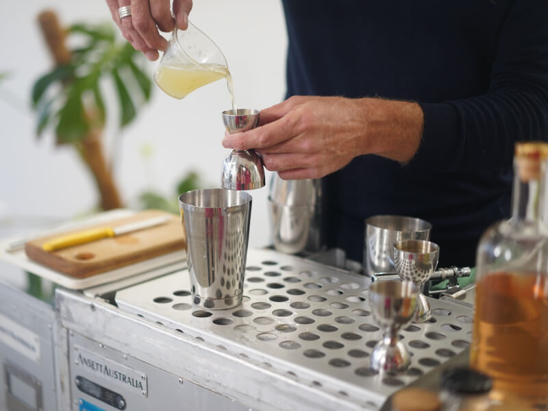 A close up of a person adding juice to a spirit measure from a glass jug