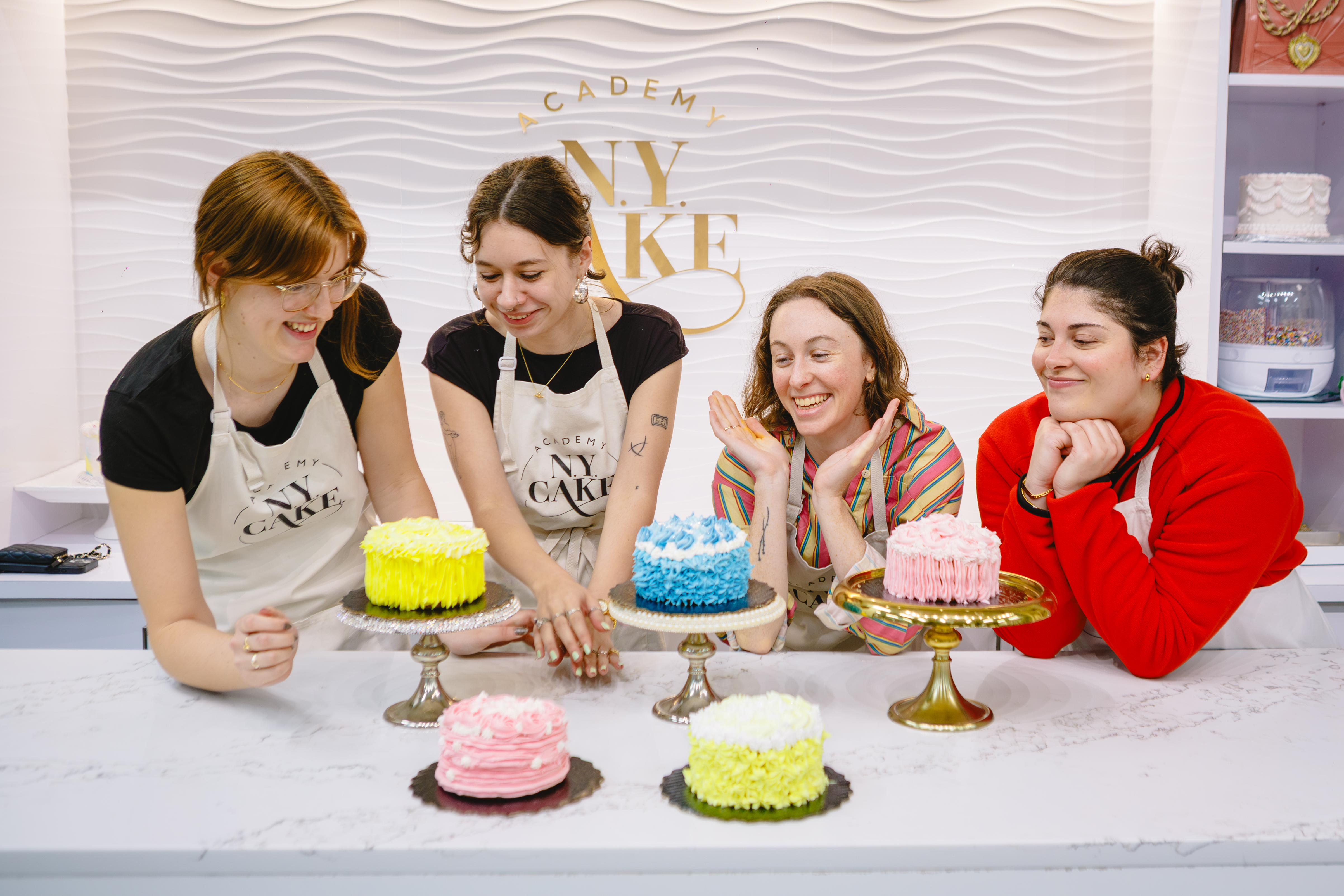 A group of people are standing in front of a row of hand decorated cakes