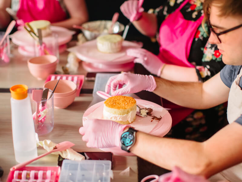 A person is applying buttercream frosting to a small sponge cake