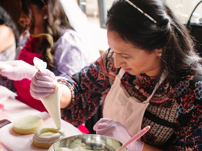 A close up of a person adding buttercream to a sponge cake