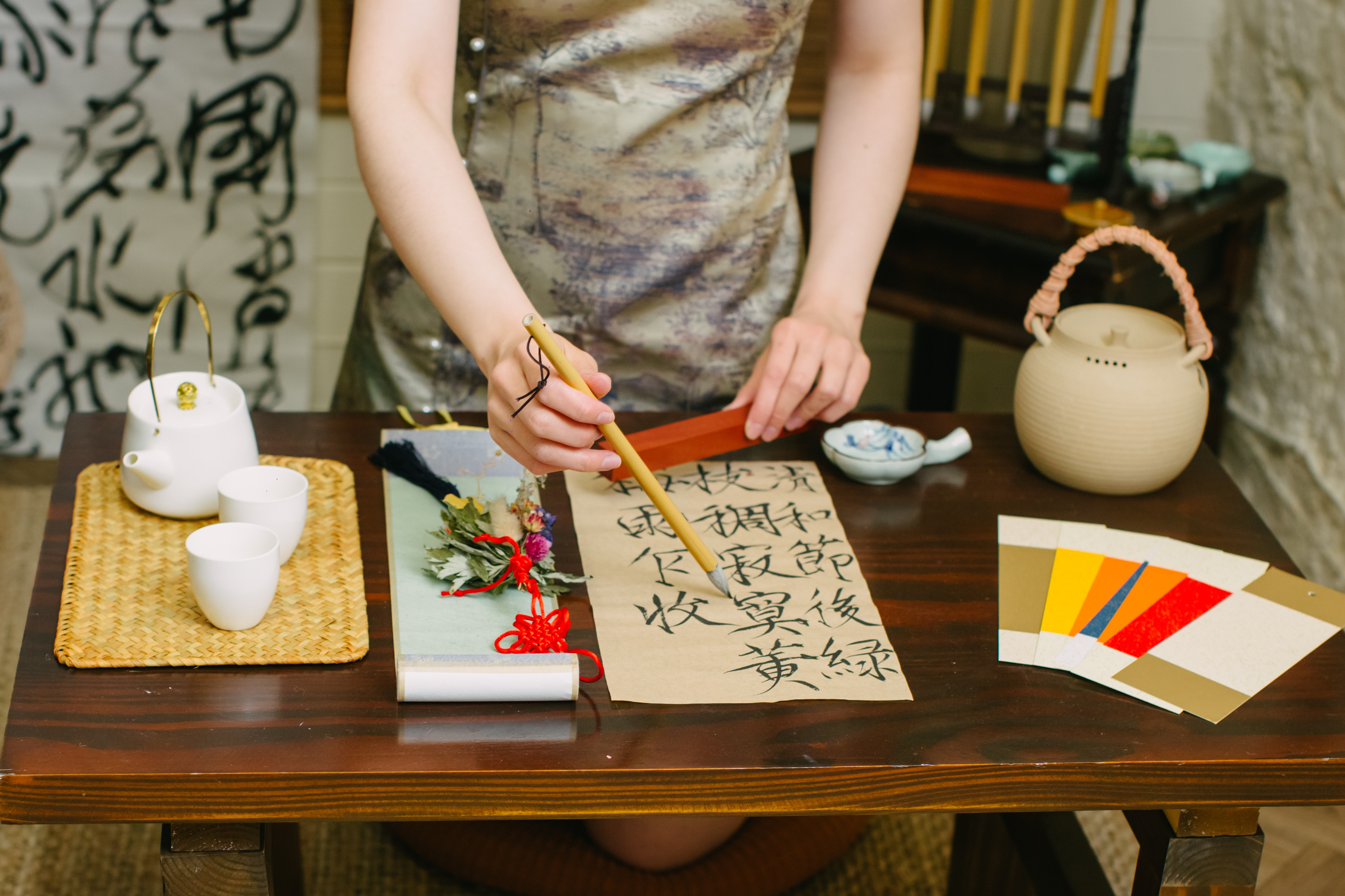 A close up of a person standing at a wooden table doing traditional calligraphy