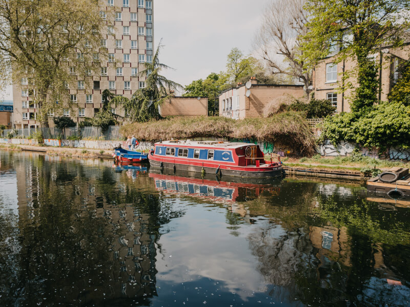 A picture of a red and blue canal boat moored in London, with city buildings in the background