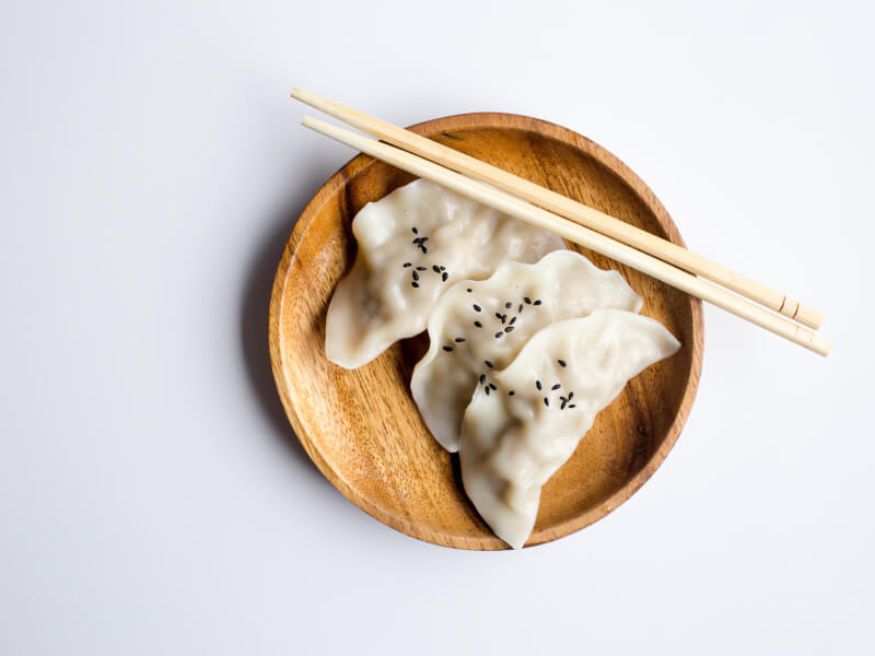 Dumplings on a wooden plate on a white table with wooden chopsticks 