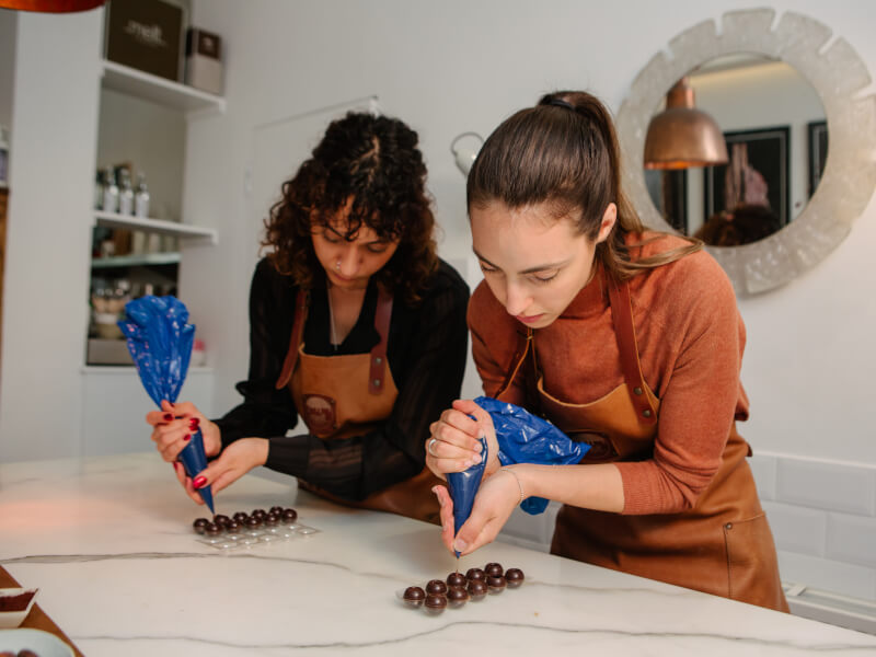 Two women are piping chocolate truffles from a piping bag