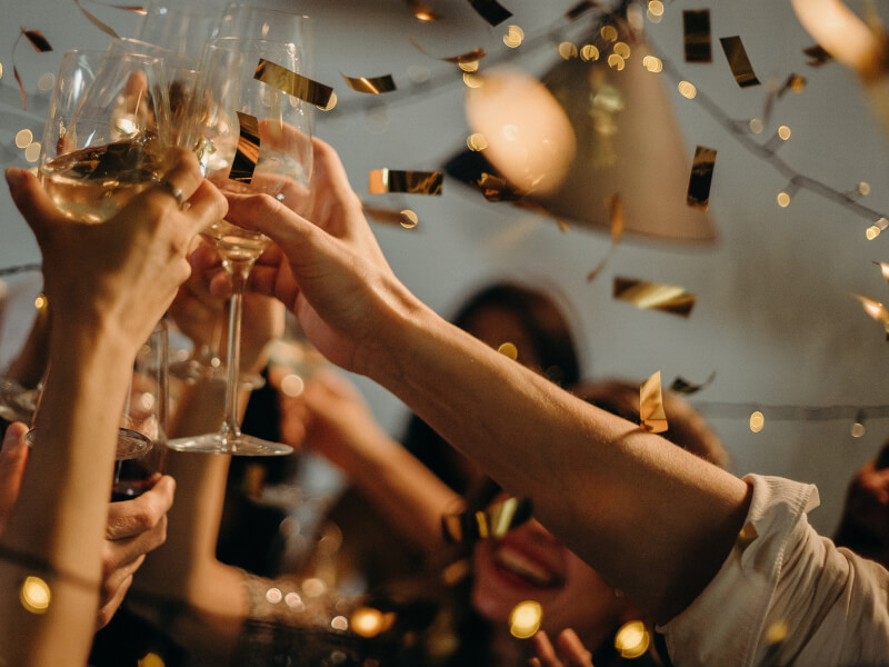 A group of people clinking wine glasses together as confetti falls from the ceiling