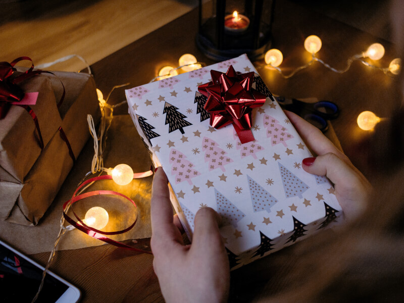A person holding a wrapped christmas present next to other wrapped presents