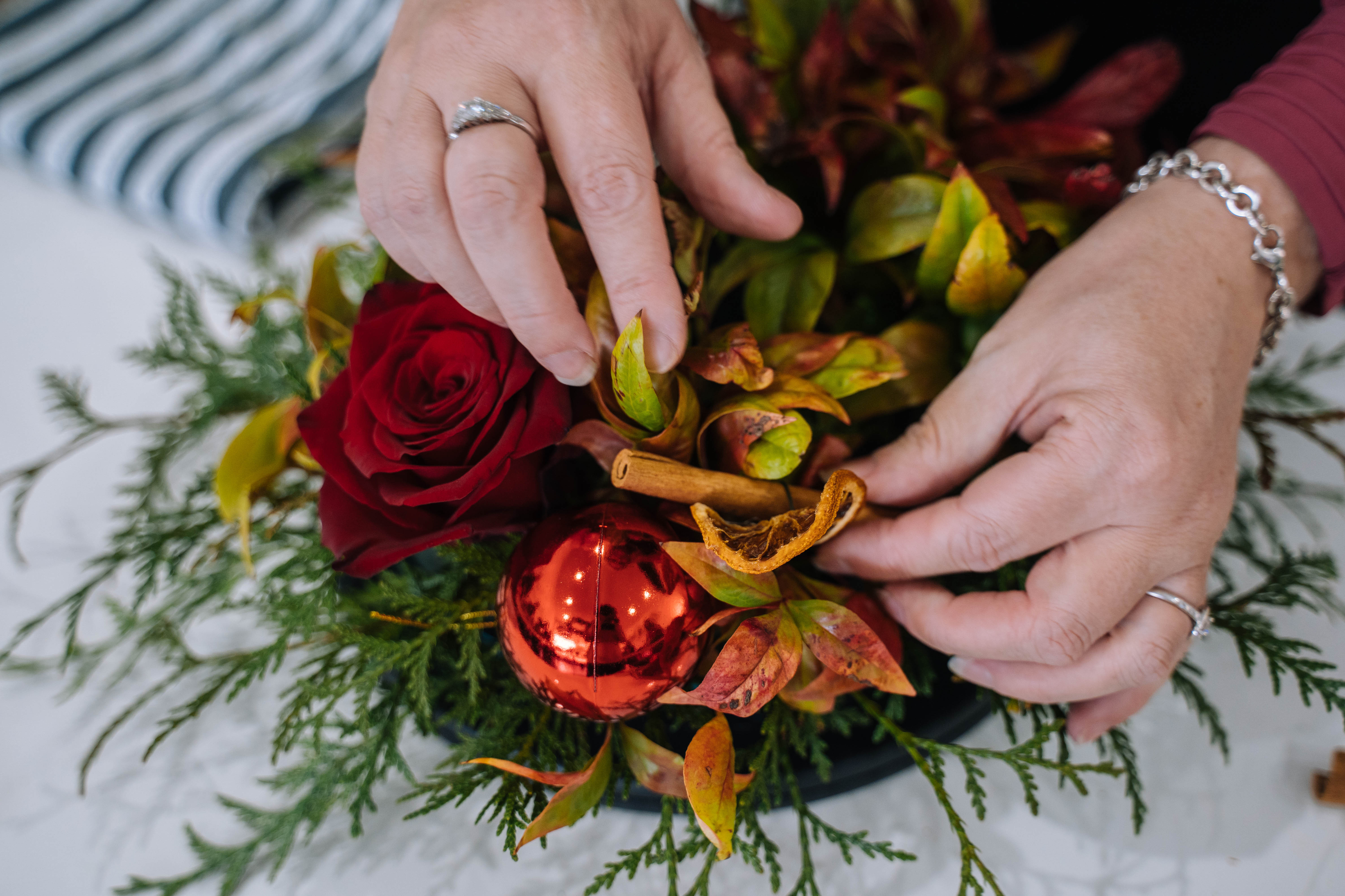 A close up of two hands adding decorations to a handmade Christmas wreath