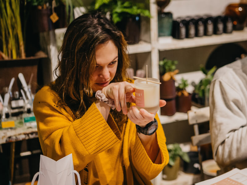A woman in a yellow jumper holds up a handmade candle 