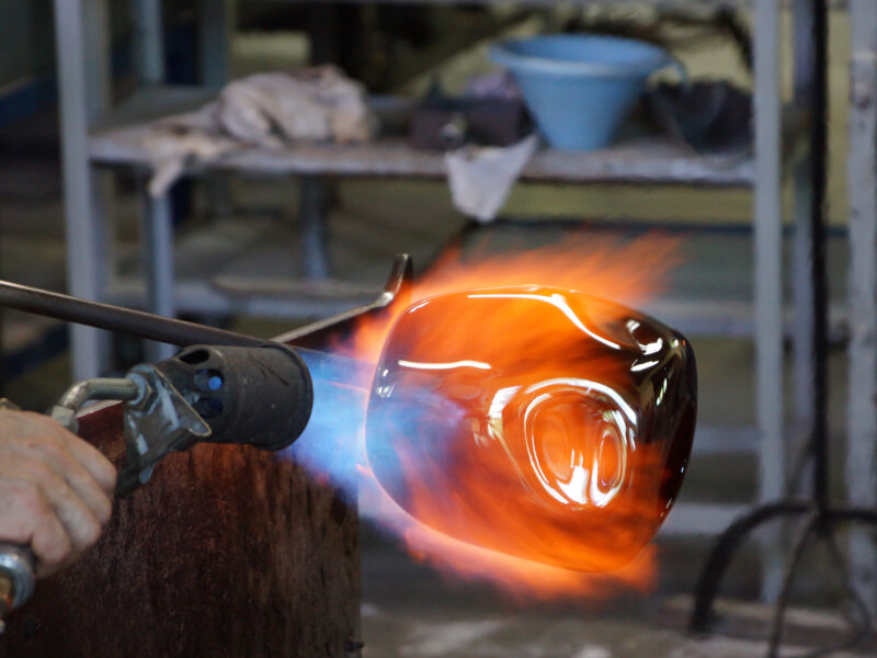 A person is using a heat tool to blow glass
