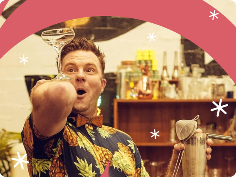 A man wearing a patterned shirt balances an empty cocktail class on his elbow