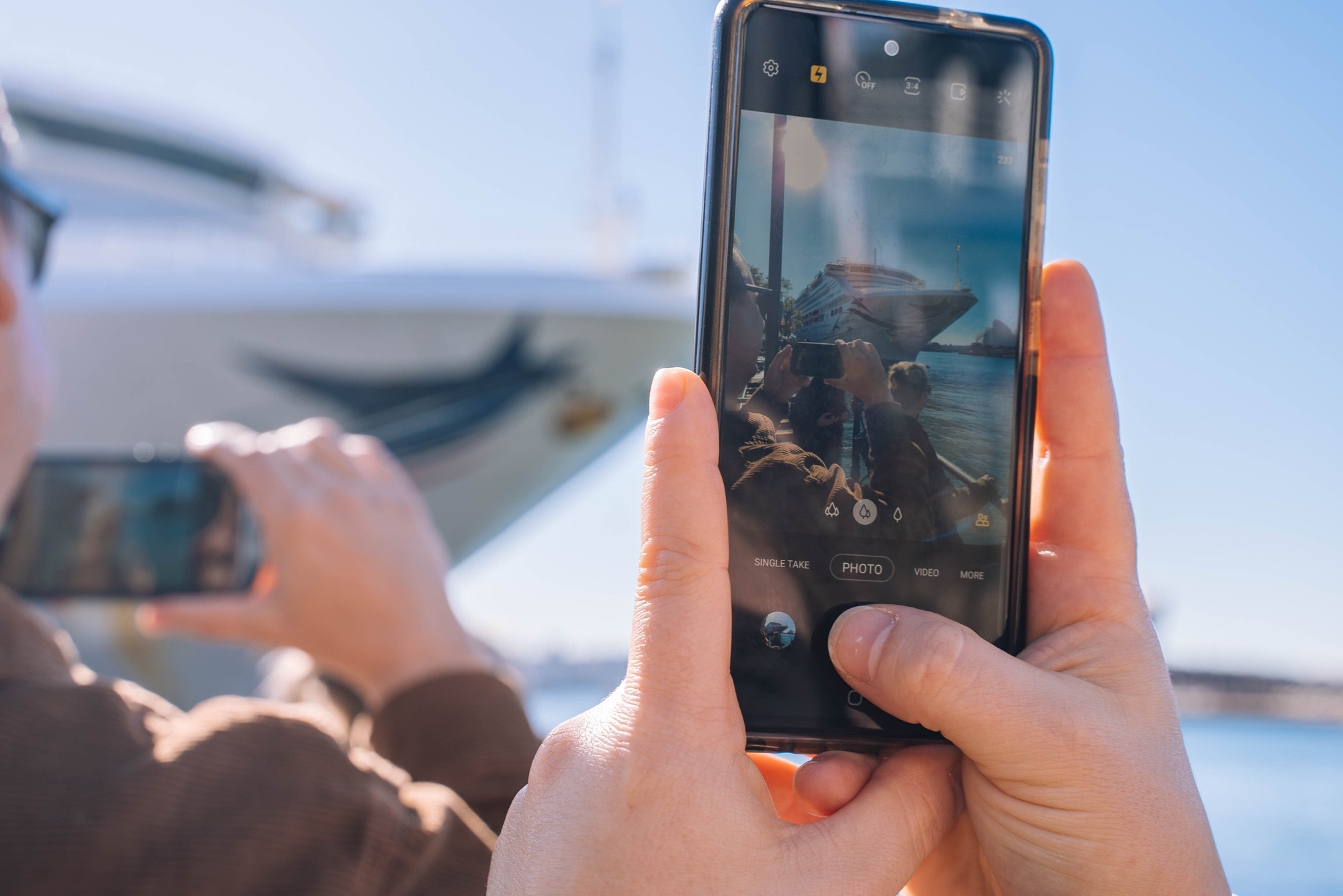 close up of hands taking a photo of a boat using a smartphone