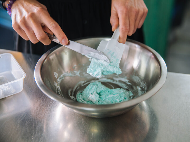 A close up of someone stirring blue mixture in a mixing bowl