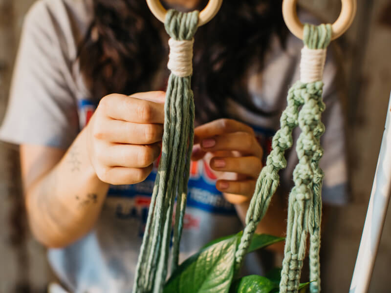 A close up of a person making a DIY plant hanger using green macrame cord