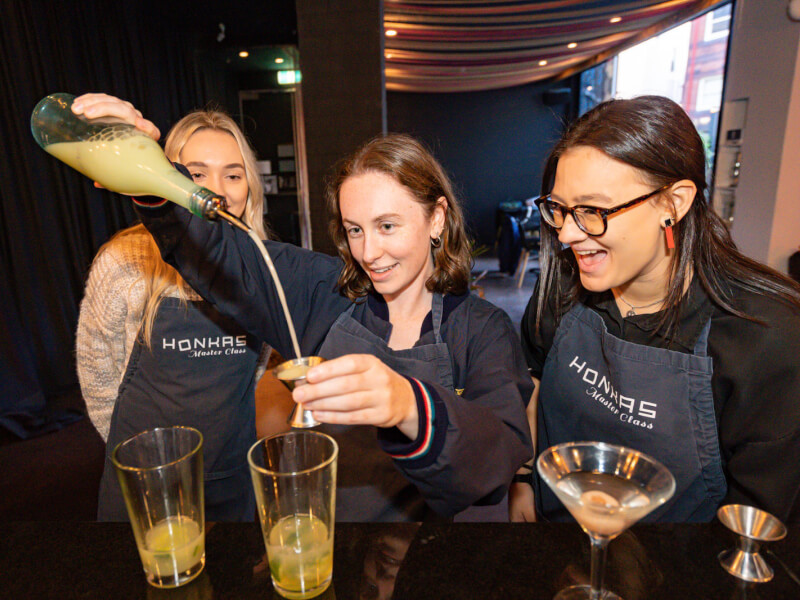 Three women are making cocktails in a bar