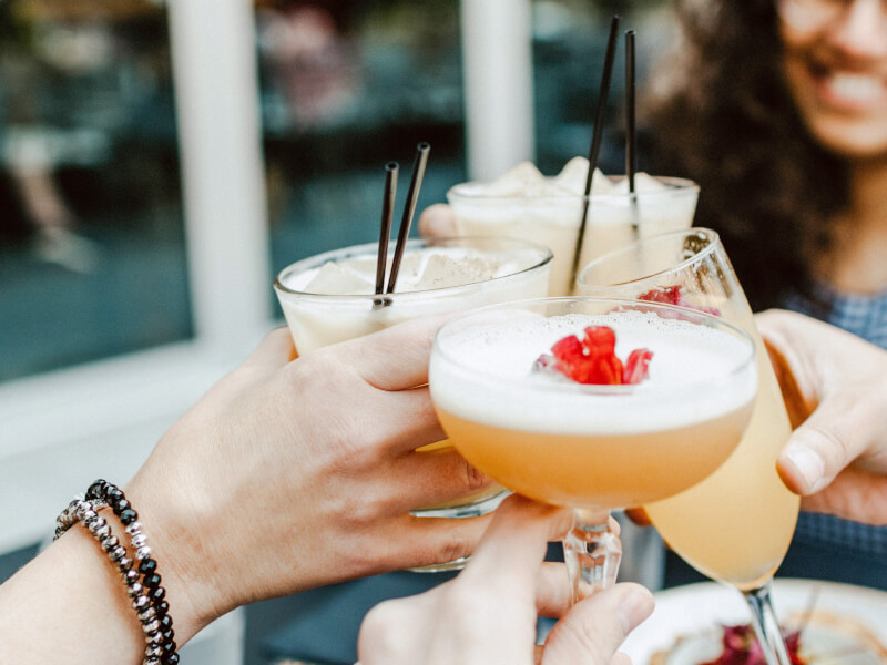 Three women are clinking glasses filled with cocktails in a 'cheers' motion