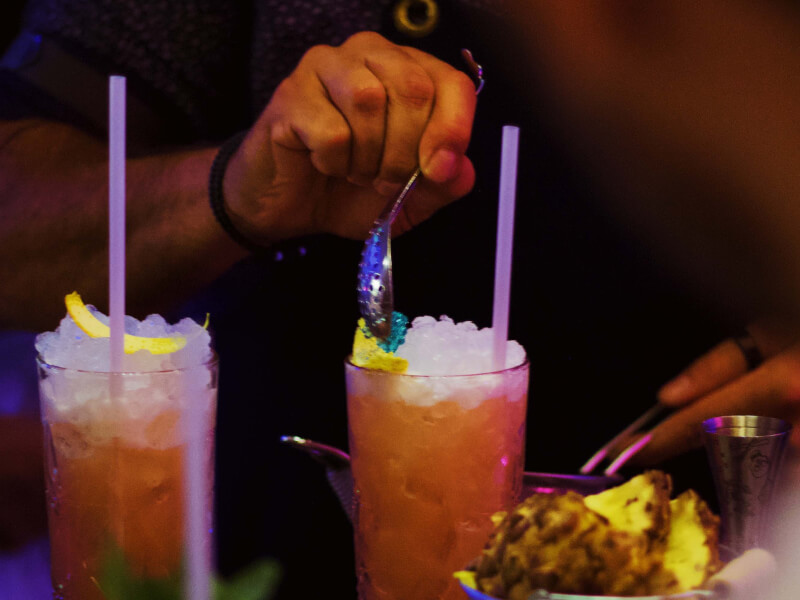 A person adding decoration to a cocktail using a metal spoon