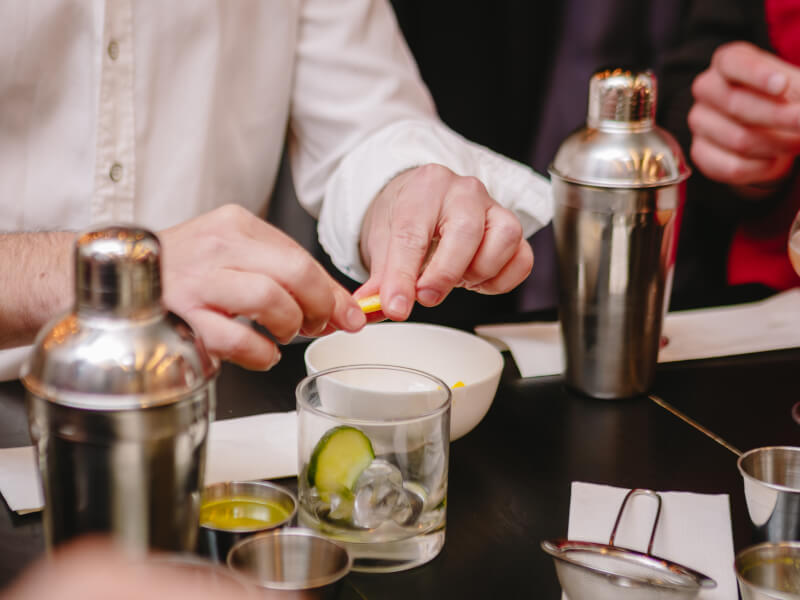 A close up of a person squeezing lemon into a small bowl, surrounded by cocktail making equipment
