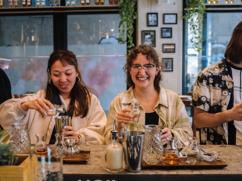 Two women are laughing and making cocktails at a mixology masterclass