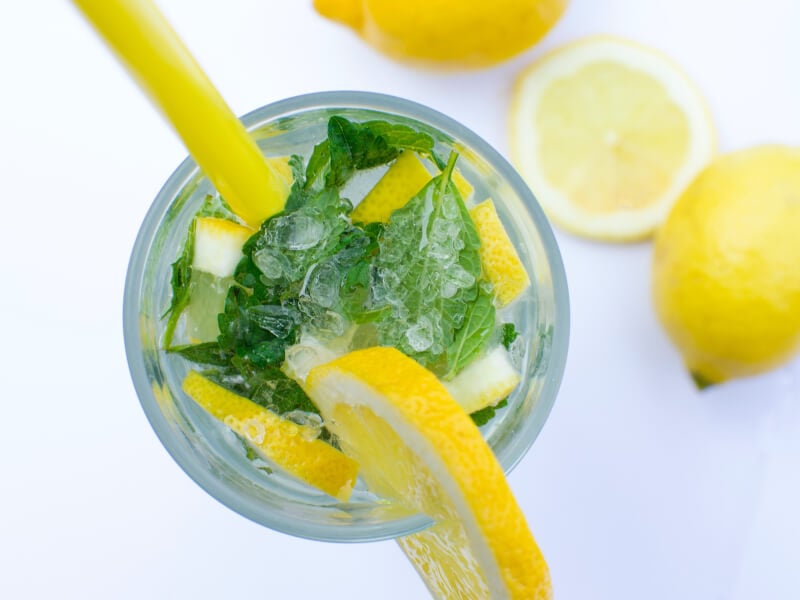 Top down view of a glass filled with ice, clear liquid, mint and lemon wedges