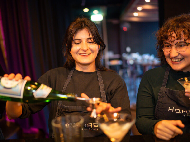 A woman is smiling and pouring spirits into a shot measure at a cocktail class
