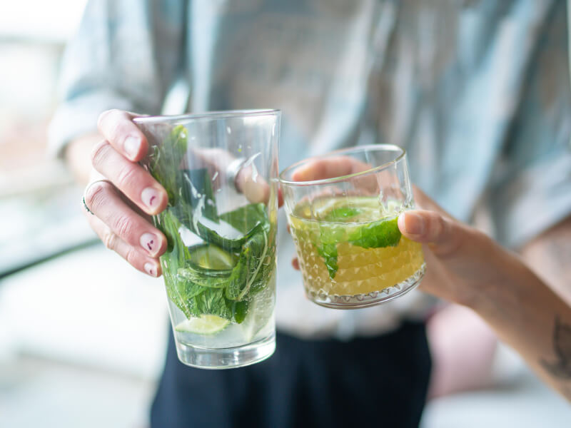 Two people clinking glasses filled with cocktails and garnishes together 