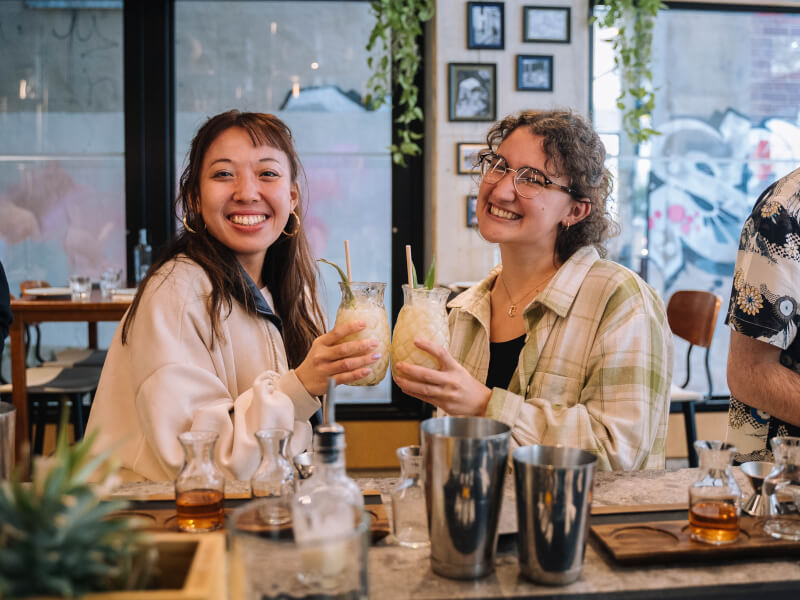 Two women smiling holding cocktails in a bar