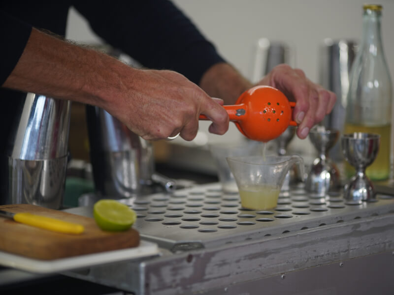 A close up of a person squeezing juice into a container to make a cocktail