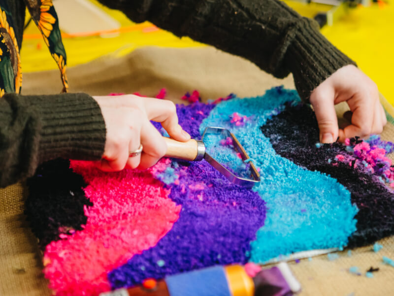 A close up of a person trimming a tufted design in colourful yarn