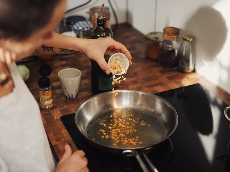 Woman pouring chopped chilli and garlic into an oiled pan during a virtual cooking class.