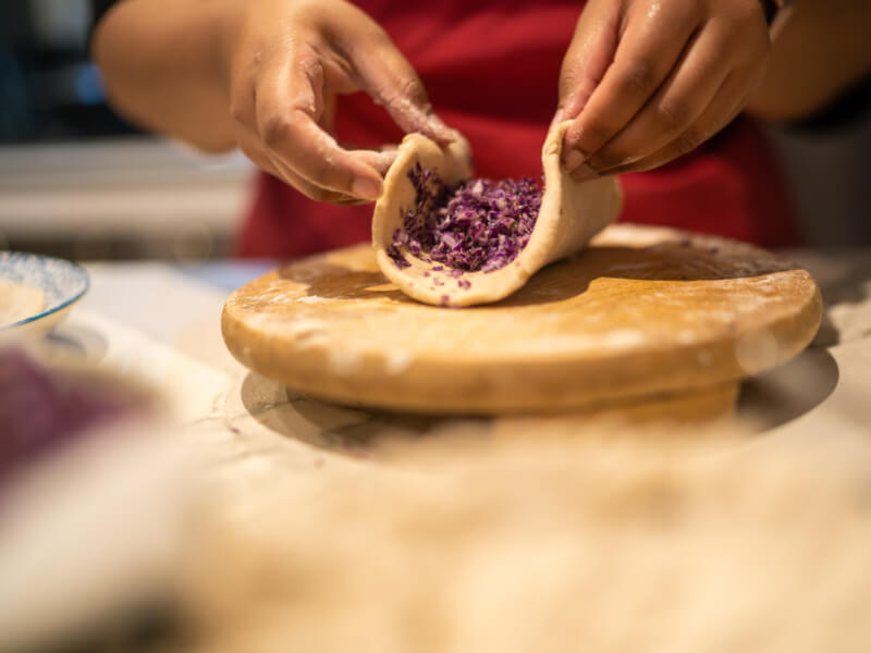 A close up of a person adding chopped vegetables to a flatbread
