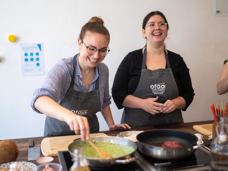 Two women are laughing and one is stirring a pan at a hen party cooking class