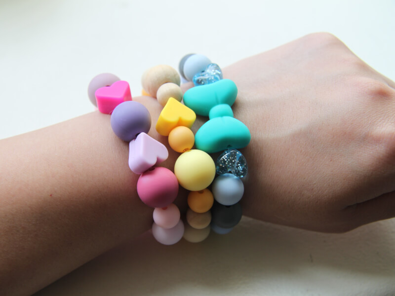 Three soft plastic DIY bracelets on a wrist with colourful heart and circular beads. 