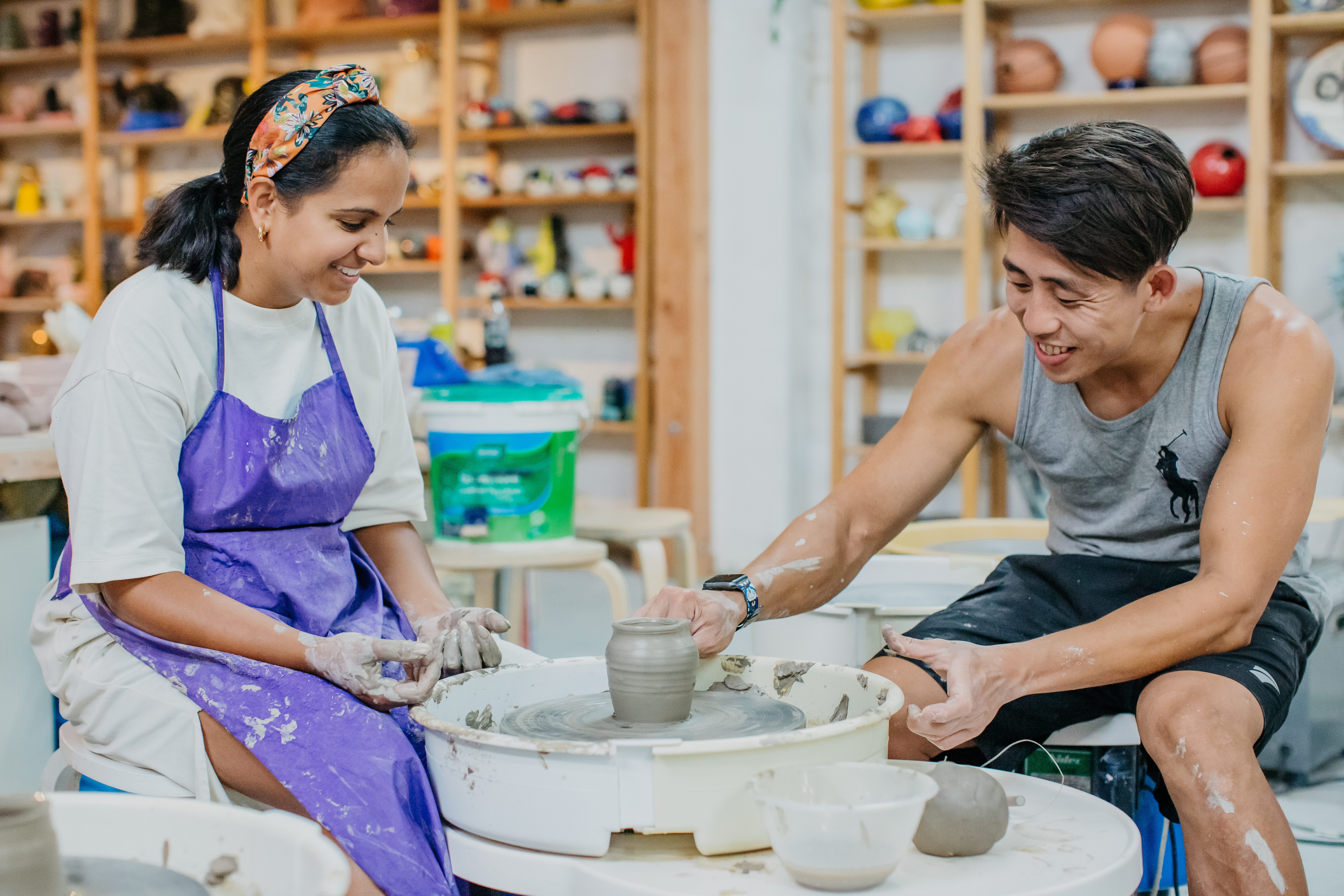 A man and woman are sitting at a pottery wheel, making a small pot