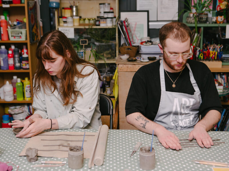 A man and woman sitting at a table rolling out clay at a hand building pottery class