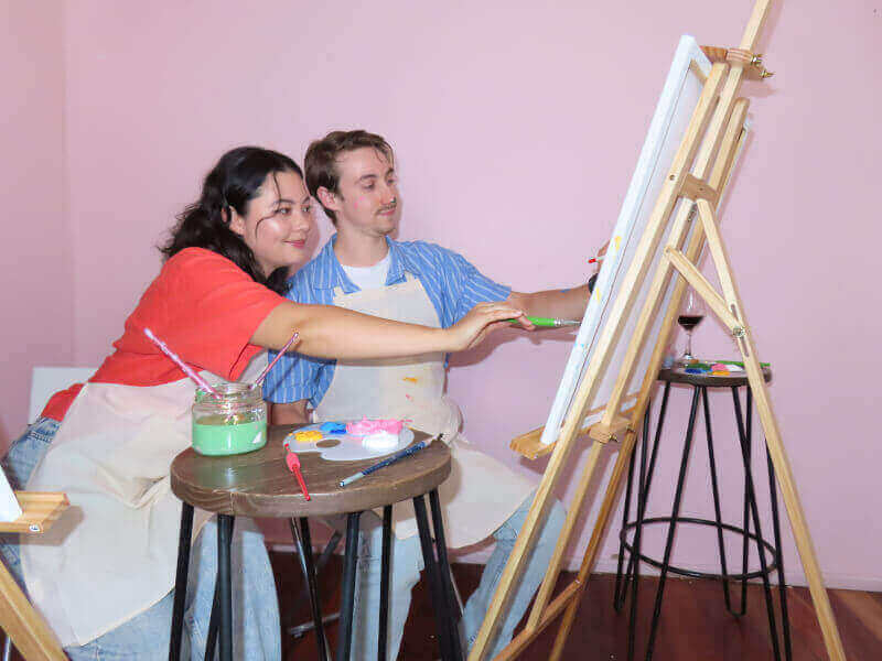 Man and woman using brushes on a canvas in a painting class