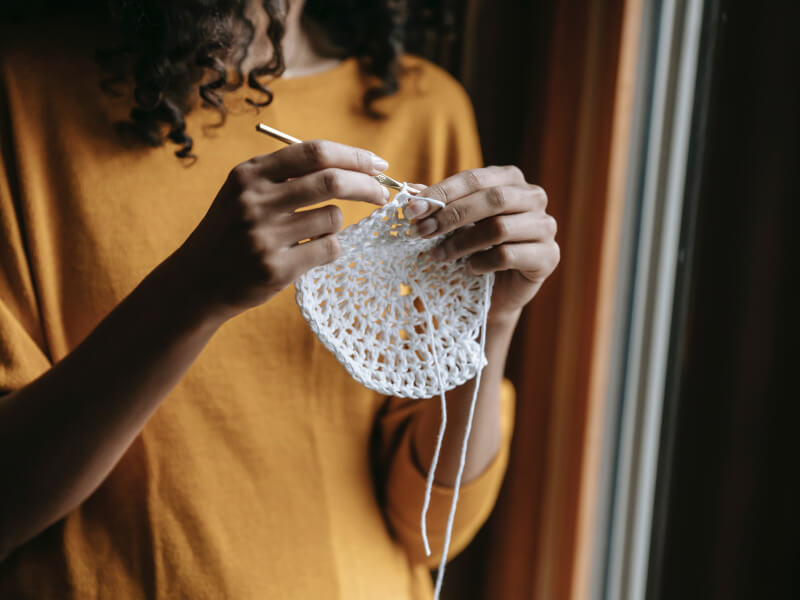 A woman is crocheting a circle using a silver crochet hook and white yarn