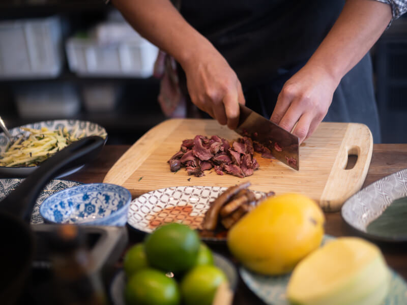 A close up of a person chopping cooked steak on a wooden board